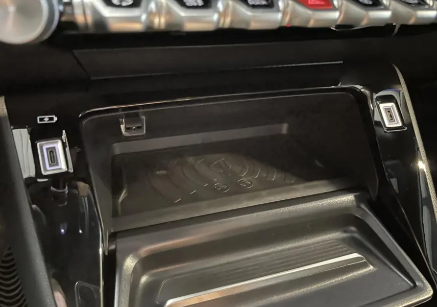 Gros plan sur la console centrale noire du Peugeot 2008 Hybrid 2026 avec chargeur à induction et prises USB type C.