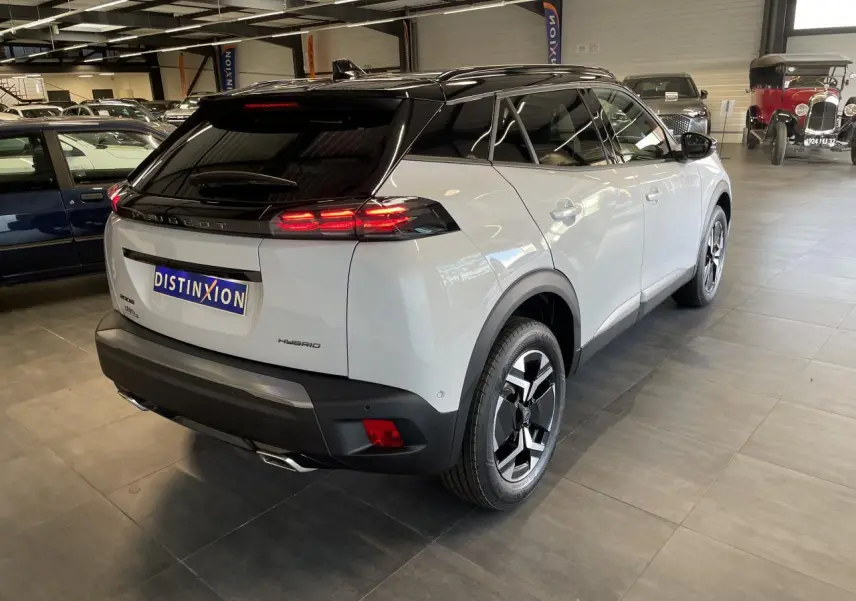 Vue 3/4 arrière droite du Peugeot 2008 blanc hybride avec toit noir et feux arrière LED en showroom.