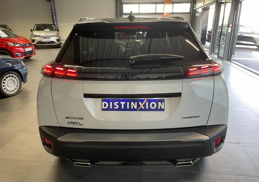 Vue arrière d'un Peugeot 2008 blanc hybride avec feux LED 3 griffes et double sortie d'échappement chromée en intérieur showroom.