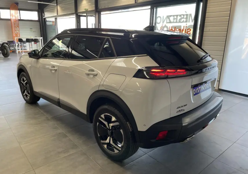 Peugeot 2008 blanc vue 3/4 arrière droit en intérieur avec toit noir et feux arrière LED allumés.