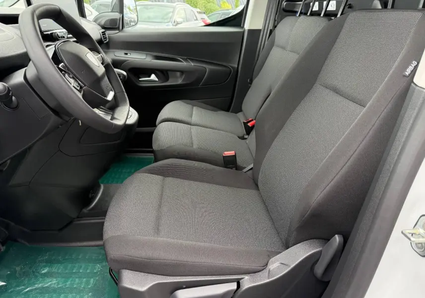 Vue intérieure côté conducteur du Peugeot Partner 2026, sièges tissu gris Curitiba Triton Meltem et volant multifonction.