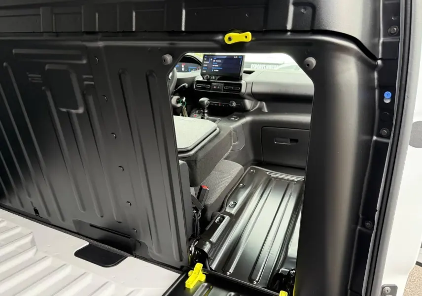 Vue intérieure par la porte latérale droite ouverte du Peugeot Partner blanc Icy, montrant la cloison et l'avant du poste de conduite.