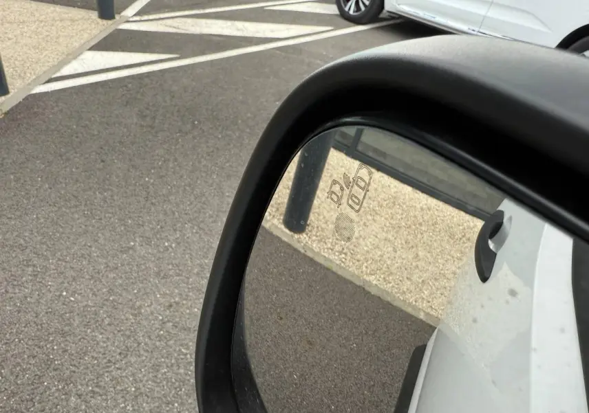 Rétroviseur extérieur côté droit d’un Peugeot Partner blanc Icy, avec détection d’angle mort visible sur le miroir.