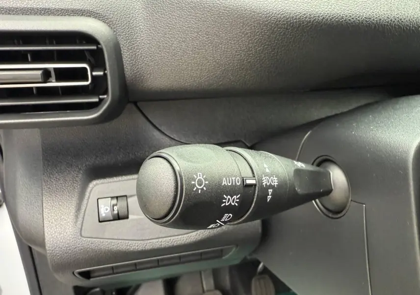 Gros plan sur la commande des phares du tableau de bord du Peugeot Partner blanc Icy, intérieur noir.
