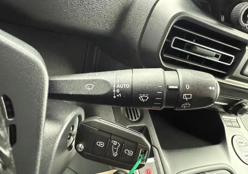 Gros plan sur la commande d’essuie-glace et la clé insérée dans le contacteur du tableau de bord noir du Peugeot Partner blanc Icy.