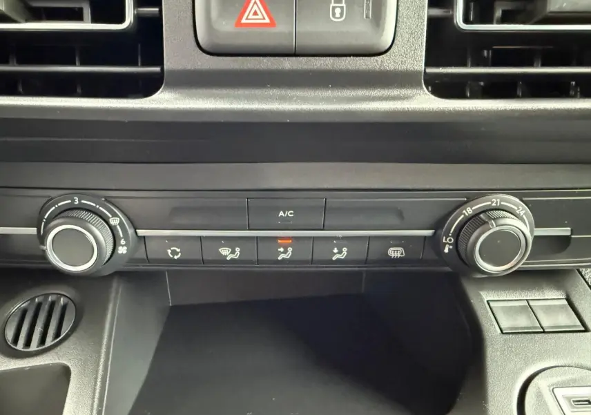 Vue rapprochée de la console centrale noire du Peugeot Partner 2026, montrant les commandes de climatisation manuelle.