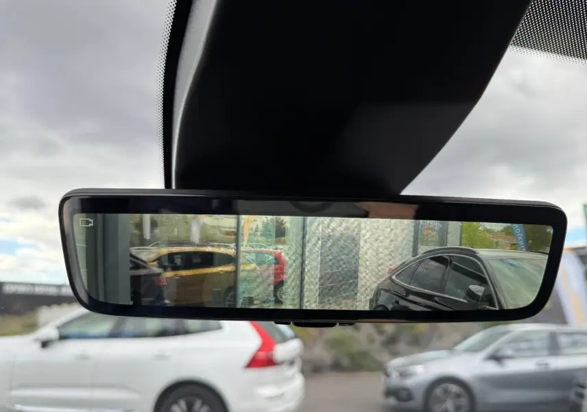 Rétroviseur intérieur numérique montrant plusieurs véhicules stationnés, avec reflet d'une voiture noire à droite.