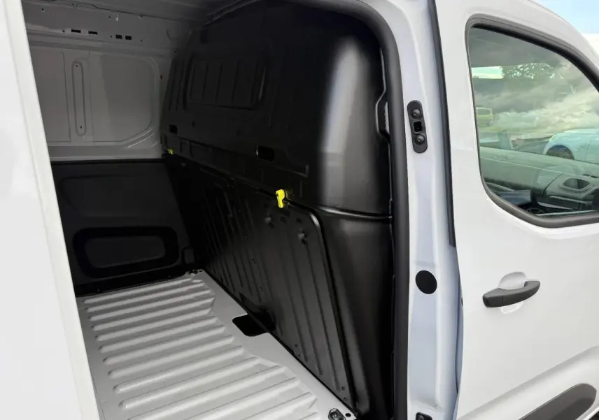 Vue intérieure côté droit du coffre d'un Peugeot Partner blanc Icy avec cloison pleine noire et porte latérale coulissante ouverte.
