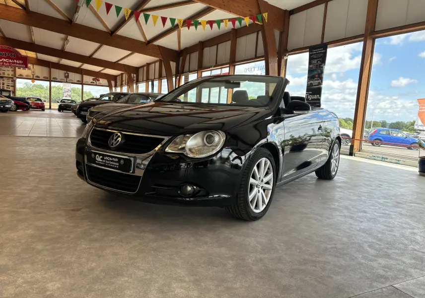 Volkswagen EOS cabriolet noir vue 3/4 avant droit dans un showroom lumineux avec toit en bois apparent.