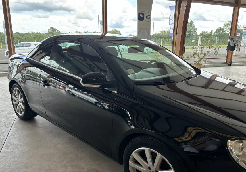 Volkswagen EOS 2008 noir brillant en vue de profil côté gauche dans un showroom lumineux avec reflets sur la carrosserie.