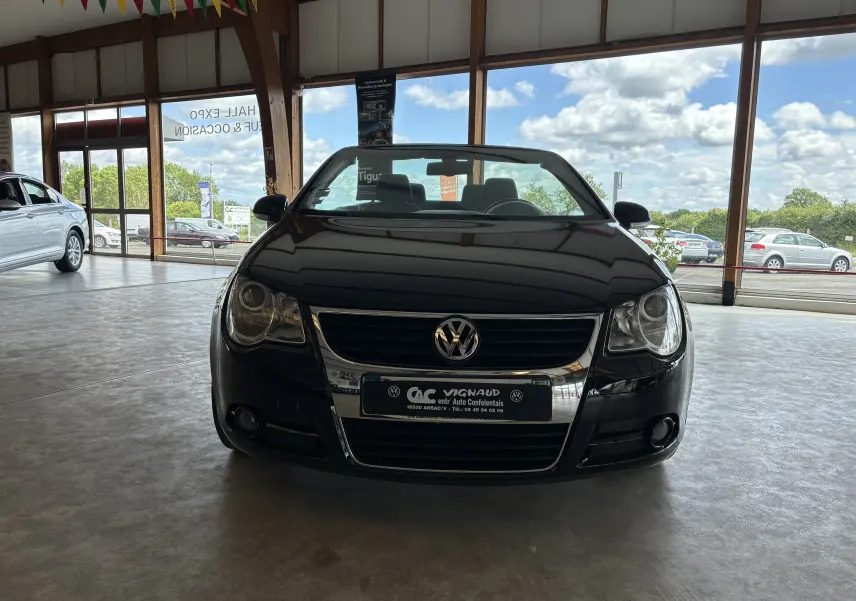 Vue de face d'une Volkswagen EOS noire en intérieur, soulignant sa calandre chromée et ses phares ronds.