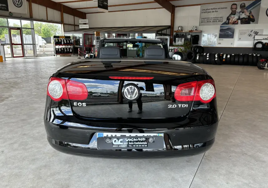 Vue arrière d'un cabriolet Volkswagen EOS noir brillant avec logo et badges 2.0 TDI visibles en intérieur showroom.