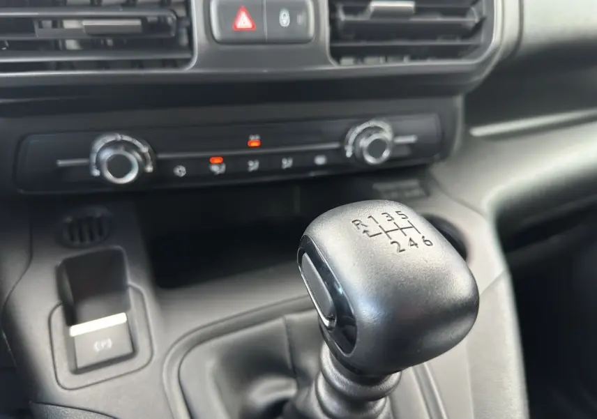 Gros plan sur le levier de vitesses manuel noir dans l'habitacle du Peugeot Partner blanc, avec commandes de climatisation visibles.