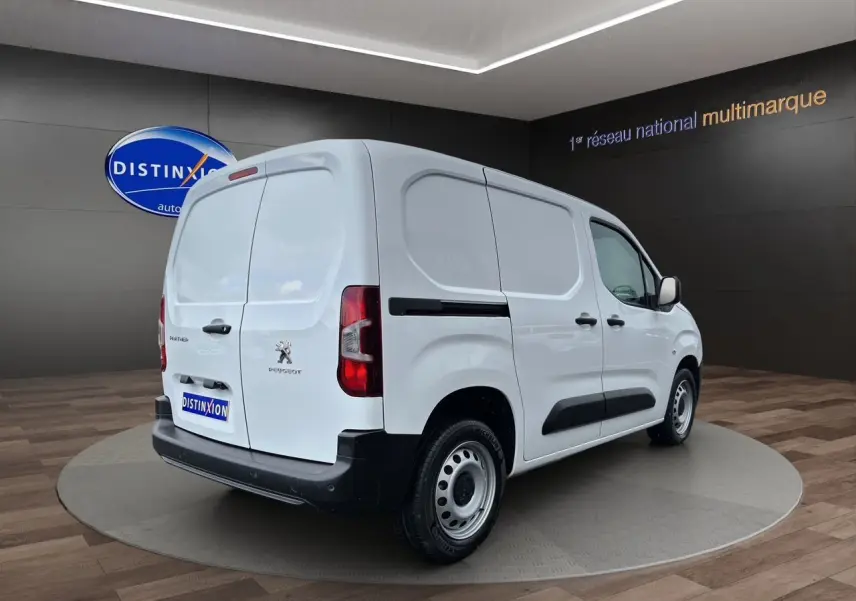 Peugeot Partner blanc en 3/4 arrière droit, utilitaire compact avec portes arrière battantes et protections latérales noires.