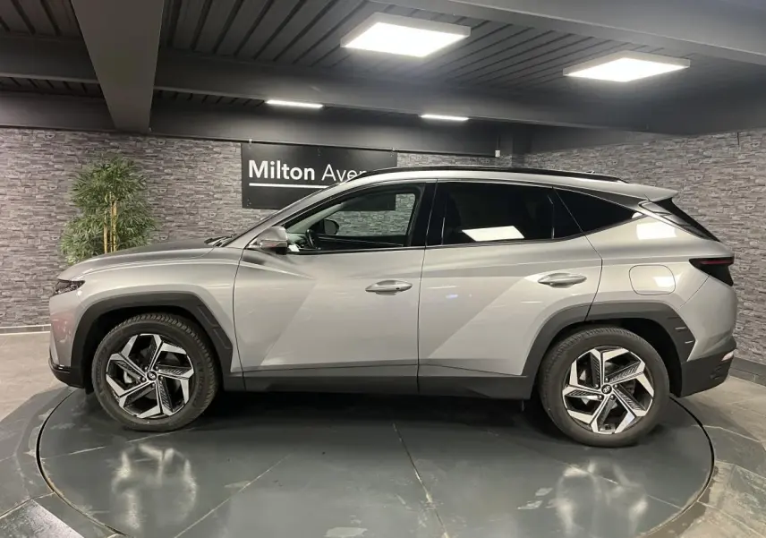 Profil côté gauche du Hyundai Tucson gris métallisé 2023 avec jantes alliage 19 pouces et toit noir contrasté.