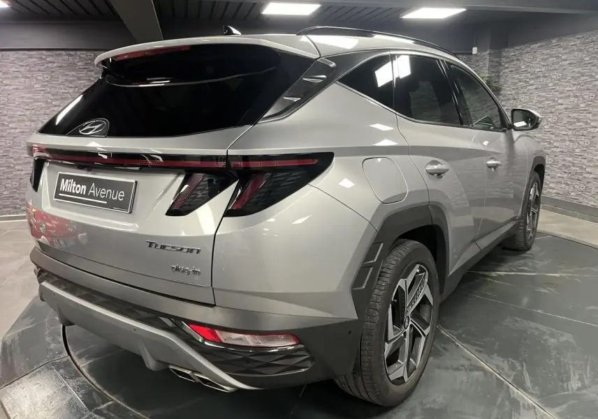 Vue 3/4 arrière droite du Hyundai Tucson gris métallisé 2023 avec feux arrière LED et double sortie d'échappement chrome.