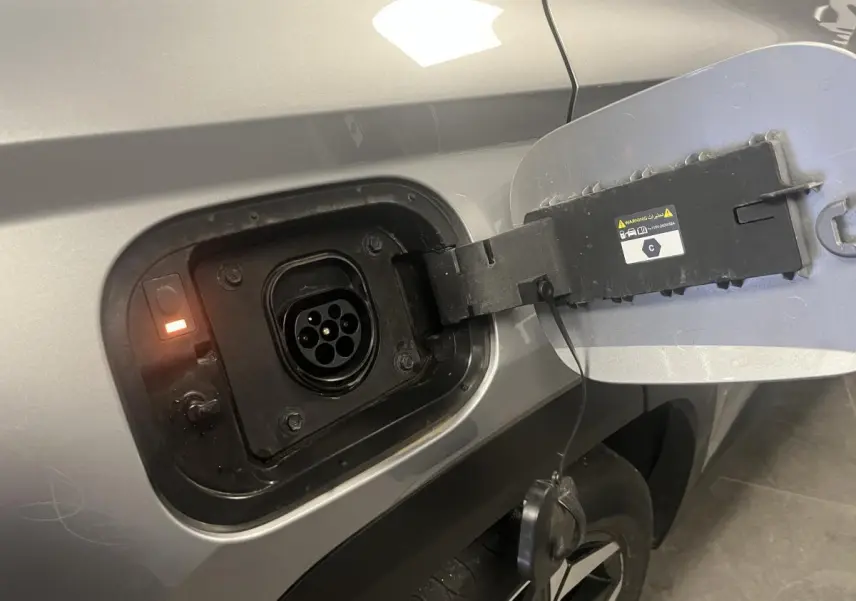 Prise de recharge ouverte côté gauche d’un Hyundai Tucson gris 2023 hybride rechargeable, avec témoin lumineux orange.