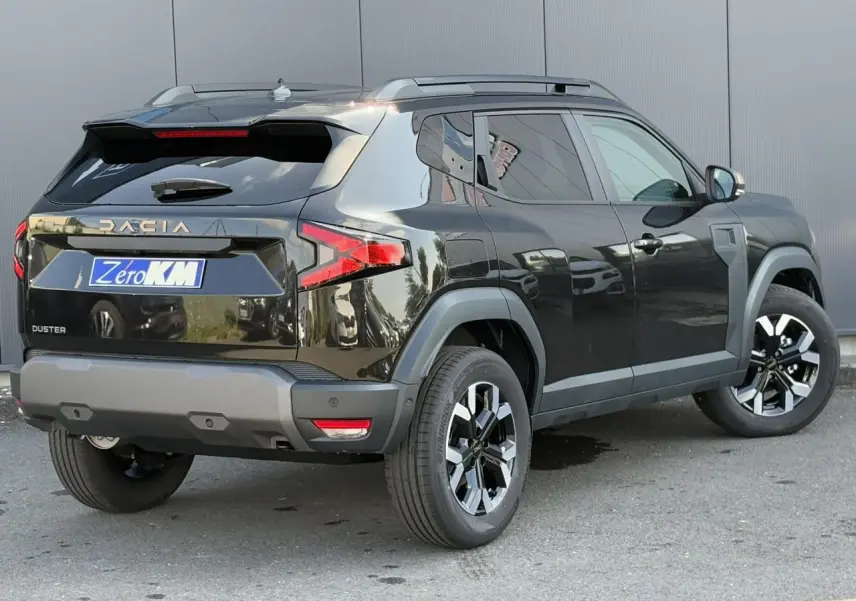 Vue 3/4 arrière droite du Dacia Duster 2025 noir nacré avec barres de toit et jantes alliage bicolores.