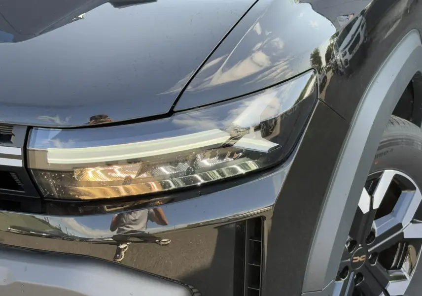 Gros plan sur le phare avant droit et la jante alliage du Dacia Duster noir nacré 2025 finition Extrême.