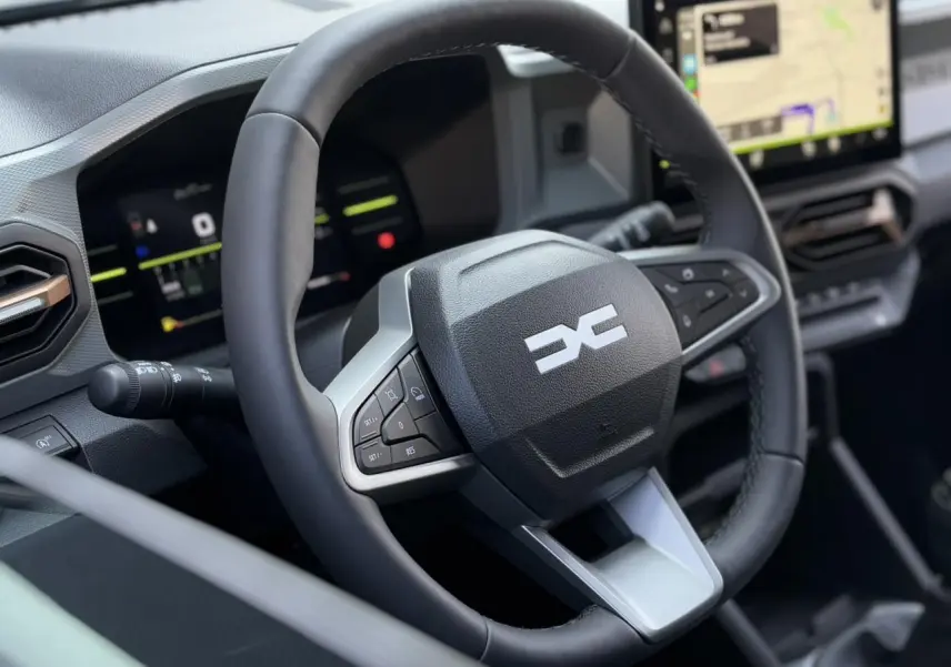 Gros plan sur le volant multifonction noir du Dacia Duster 2025 avec tableau de bord digital et écran GPS tactile.