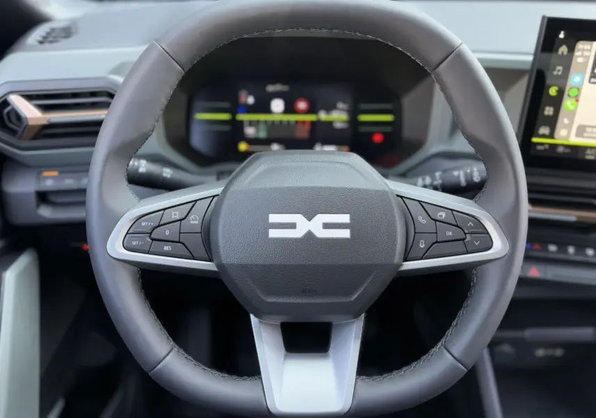 Vue rapprochée du volant noir du Dacia Duster 2025 avec commandes intégrées et tableau de bord digital en arrière-plan.