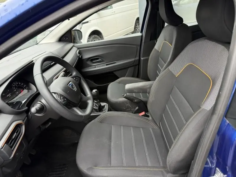 Intérieur avant côté conducteur d'une Dacia Sandero Stepway bleu métal 2022, sièges noirs avec surpiqûres jaunes.
