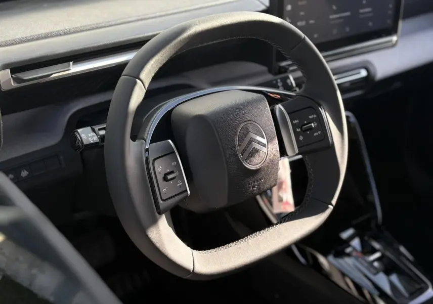 Vue rapprochée du volant multifonctions noir de la Citroën C3 Aircross 2025, avec tableau de bord gris et écran tactile visible.