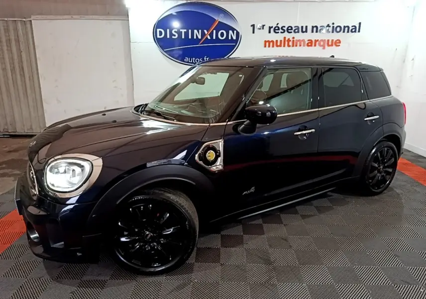Vue 3/4 avant droit d'une MINI Countryman Cooper SE bleu foncé avec jantes noires et toit noir dans un showroom.