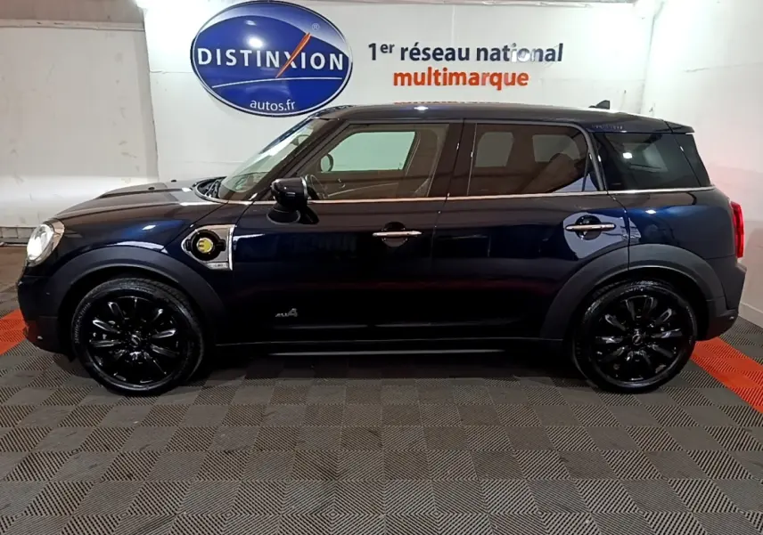 Profil côté gauche d'un MINI Countryman Cooper SE bleu avec jantes noires et badge hybride visible sur l'aile avant.