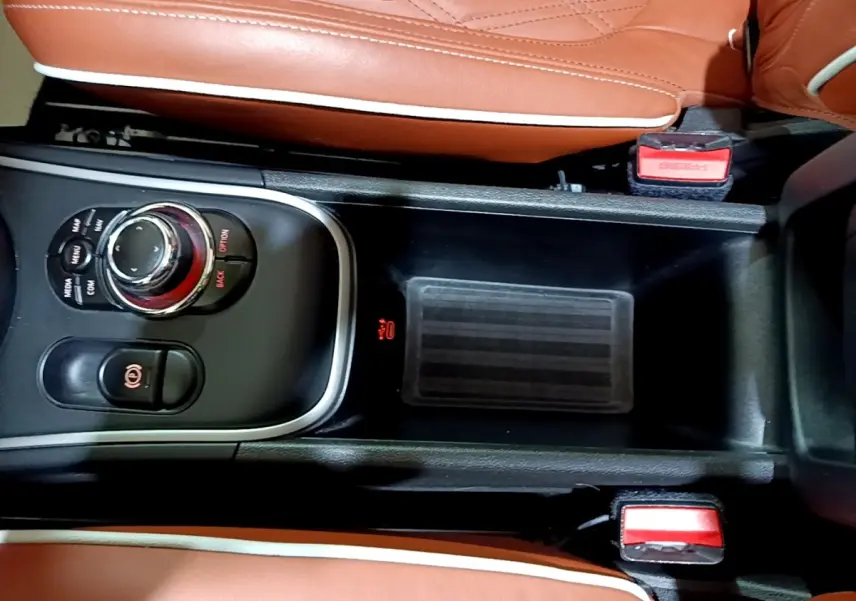 Vue rapprochée de la console centrale noire avec molette de commande et sièges en cuir marron clair du MINI Countryman hybride.