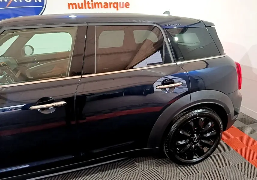 Profil côté gauche d'une MINI Countryman bleu foncé avec jantes noires brillantes dans un showroom intérieur.