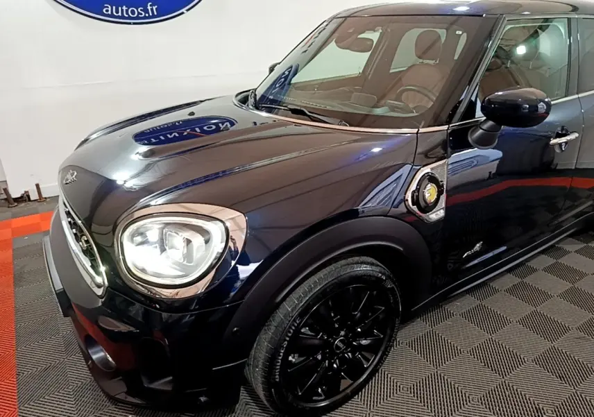 Vue 3/4 avant droit d'une MINI Countryman Cooper SE hybride rechargeable bleu foncé avec jantes noires et logo électrique sur l'aile.