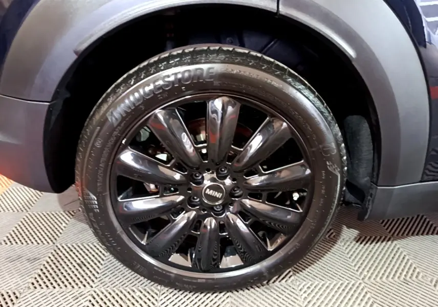 Gros plan sur la roue avant droite noire brillante du MINI Countryman Cooper SE hybride bleu, avec logo MINI central.