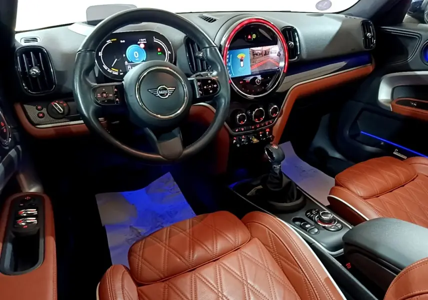 Vue intérieure avant du MINI Countryman Cooper SE avec sièges cuir marron et tableau de bord numérique éclairé.