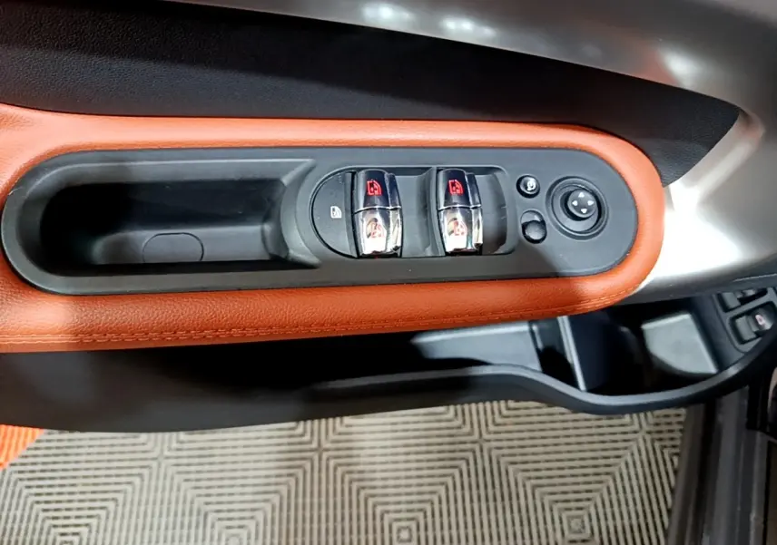 Gros plan sur les commandes de lève-vitres chromées et cadre orange sur la porte côté conducteur d'un MINI Countryman bleu.