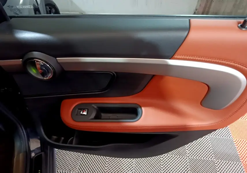 Gros plan sur la porte intérieure côté gauche du MINI Countryman bleu, avec garniture cuir marron et poignée argentée.