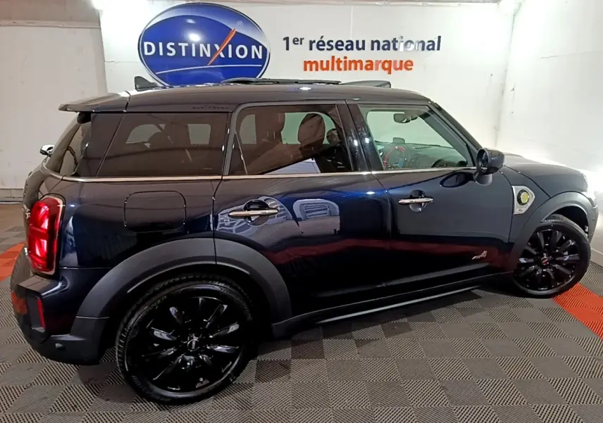 Vue latérale droite d'un MINI Countryman Cooper SE bleu avec jantes noires et toit foncé en intérieur showroom.