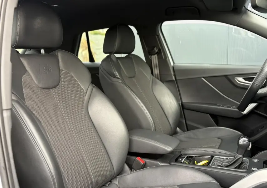 Vue intérieure côté conducteur de l'Audi Q2 S-Line 35 TDI 150 avec sièges sport cuir/tissu noirs et console centrale.
