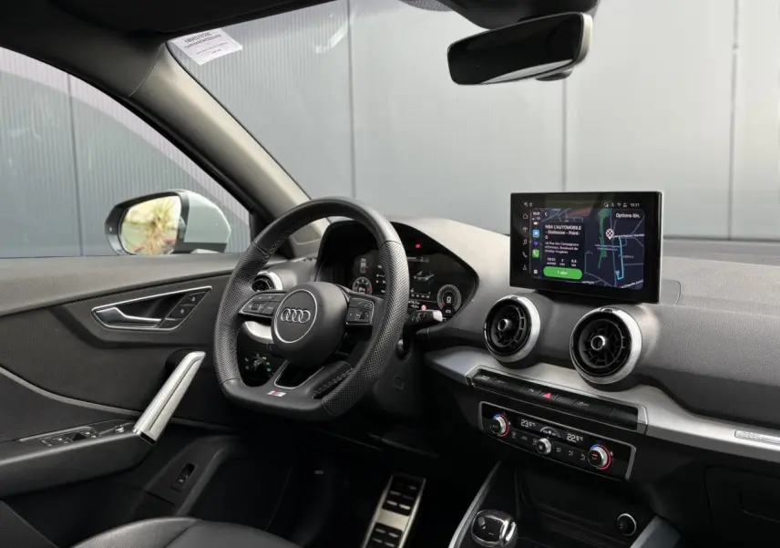 Vue intérieure côté conducteur de l'Audi Q2 S-Line 2025, volant cuir, écran MMI navigation et pédales acier inoxydable.