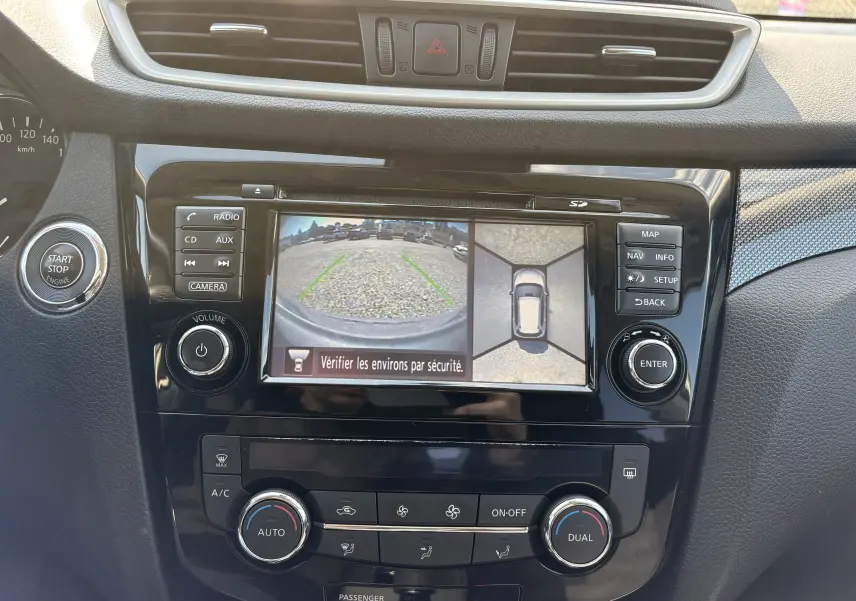 Tableau de bord du Nissan X-TRAIL 2016 avec écran de caméra de recul et commandes de climatisation visibles.