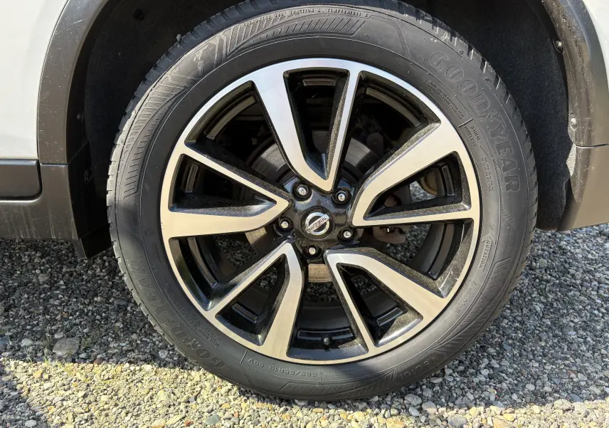Gros plan sur la roue avant gauche du Nissan X-TRAIL 2016 blanc, jante alliage noir et argent avec pneu Goodyear.