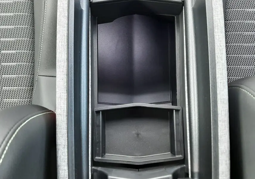 Vue plongeante sur la console centrale ouverte du Peugeot 3008 gris titane, montrant le rangement intérieur et les sièges tissu noir.