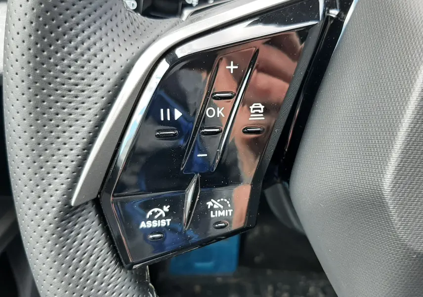 Gros plan sur les commandes noires du volant perforé côté gauche du Peugeot 3008 gris titane hybride 2026.