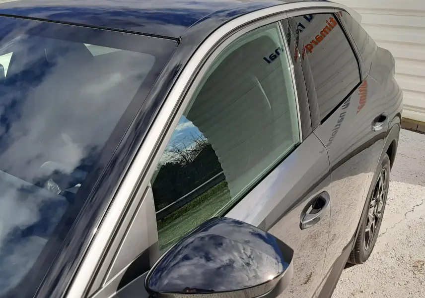 Vue de côté droit avant du Peugeot 3008 gris titane avec toit et rétroviseur noir brillant, reflet du ciel visible.