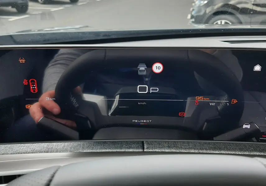 Vue rapprochée du tableau de bord numérique du Peugeot 3008 hybride gris titane, affichant la vitesse et alertes.