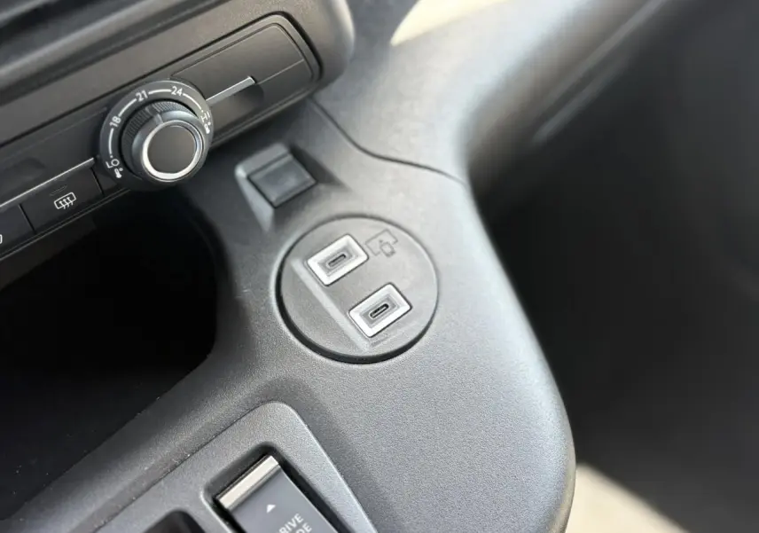 Gros plan sur la console centrale intérieure du Citroën Berlingo ë-136 bleu Kiama, montrant les ports USB et le bouton de réglage.