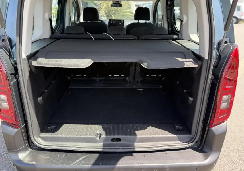 Coffre ouvert vu de l'arrière d'un Citroën Berlingo ë-136 bleu Kiama avec cache-bagages et sièges arrière rabattus.