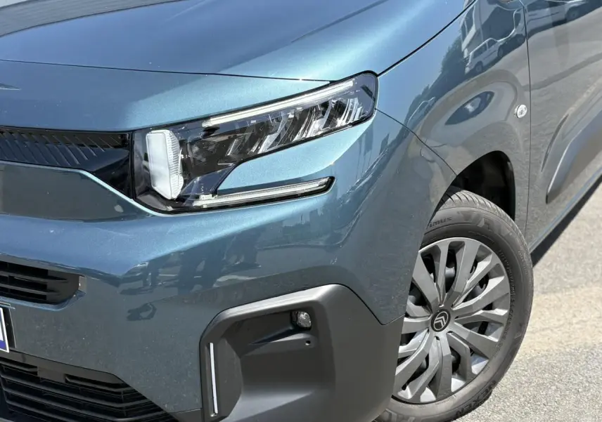 Gros plan sur l’avant droit du Citroën Berlingo ë-136 bleu Kiama, mettant en valeur le phare LED et la jante tôlée avec enjoliveur.