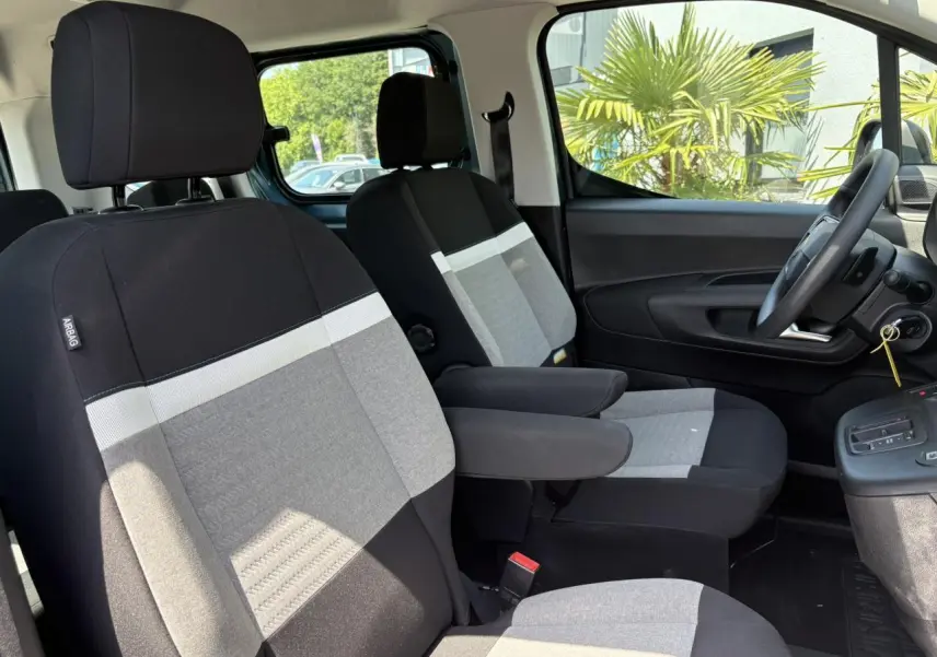 Vue intérieure côté conducteur du Citroën Berlingo ë-136 2025, sièges tissu Urban Grey avec accoudoirs.