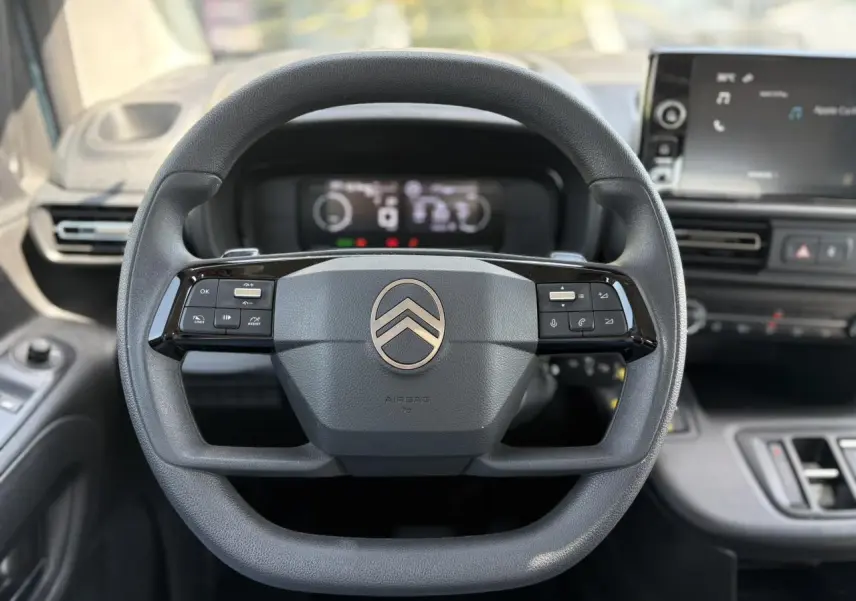 Vue frontale du volant multifonction noir du Citroën Berlingo ë-136 avec tableau de bord numérique et écran tactile.